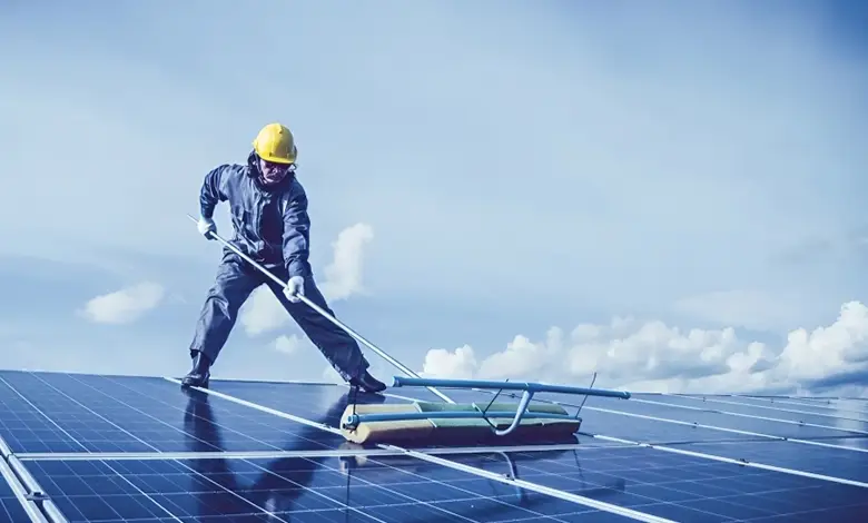 Worker Performing Solar Panel Cleaning on a Rooftop Under a Clear Sky